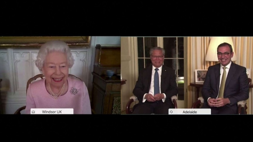 An elderly woman in pearls and a pink jacket, on a video call with two men in suits and ties.