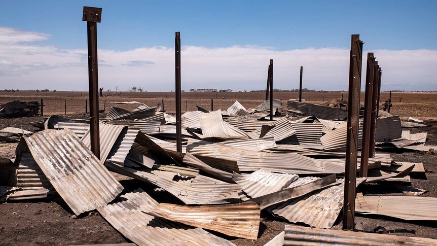 Burnt corrugated iron lays on the ground with steel vertical beams surrounding.