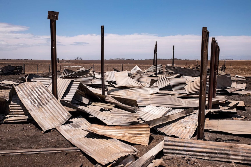 Burnt corrugated iron lays on the ground with steel vertical beams surrounding.
