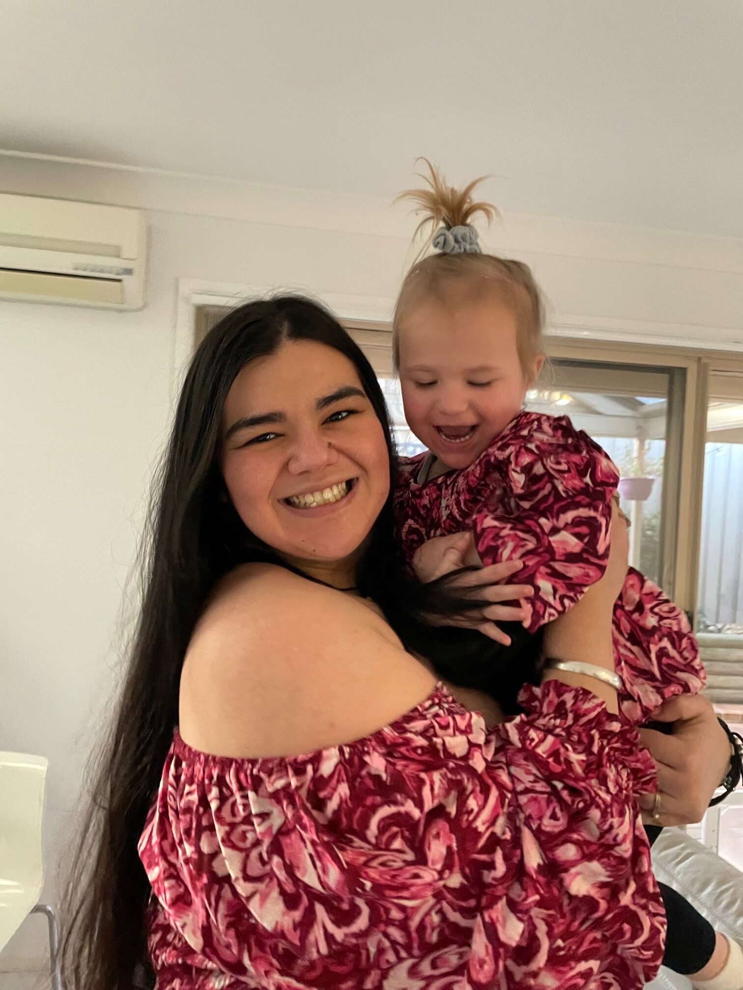 A woman smiles as she holds her thre-year-old daughter.