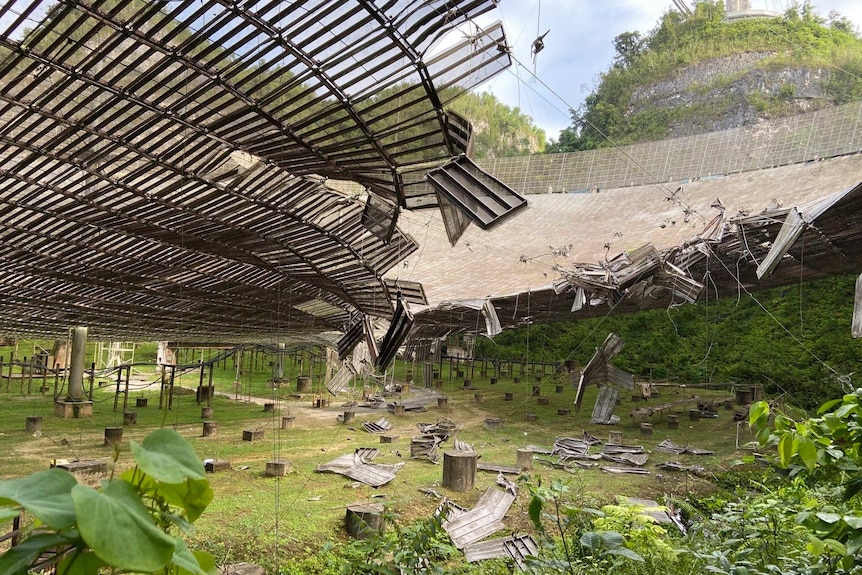 Wreckage is seen in a wide gash in the dish of the Arecibo telescope, littered with foliage and overgrowth