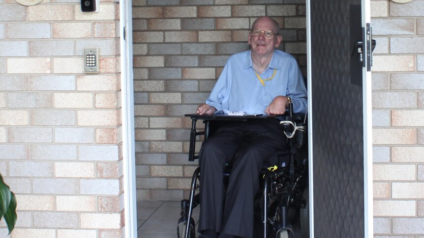 A man in a blue shirt in a wheelchair in the door way of a brick home
