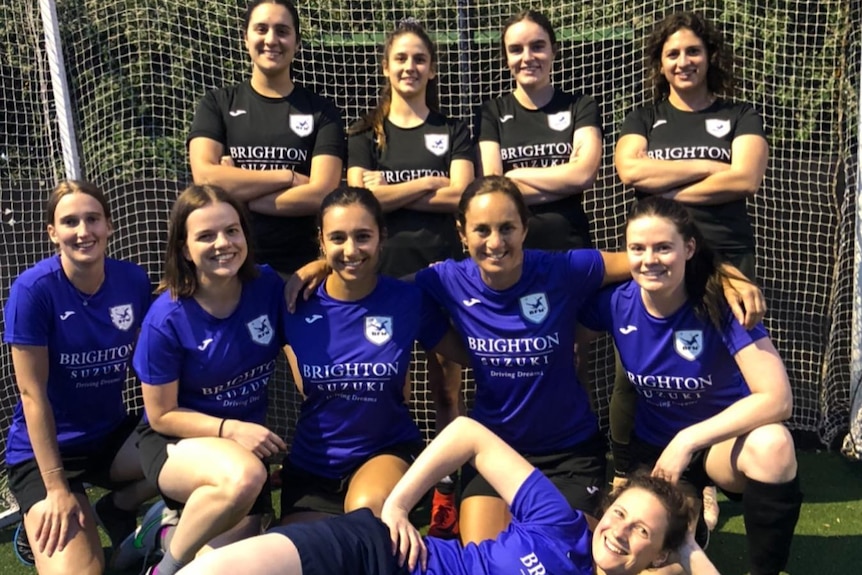 A group of women gather in front of a soccer goal.