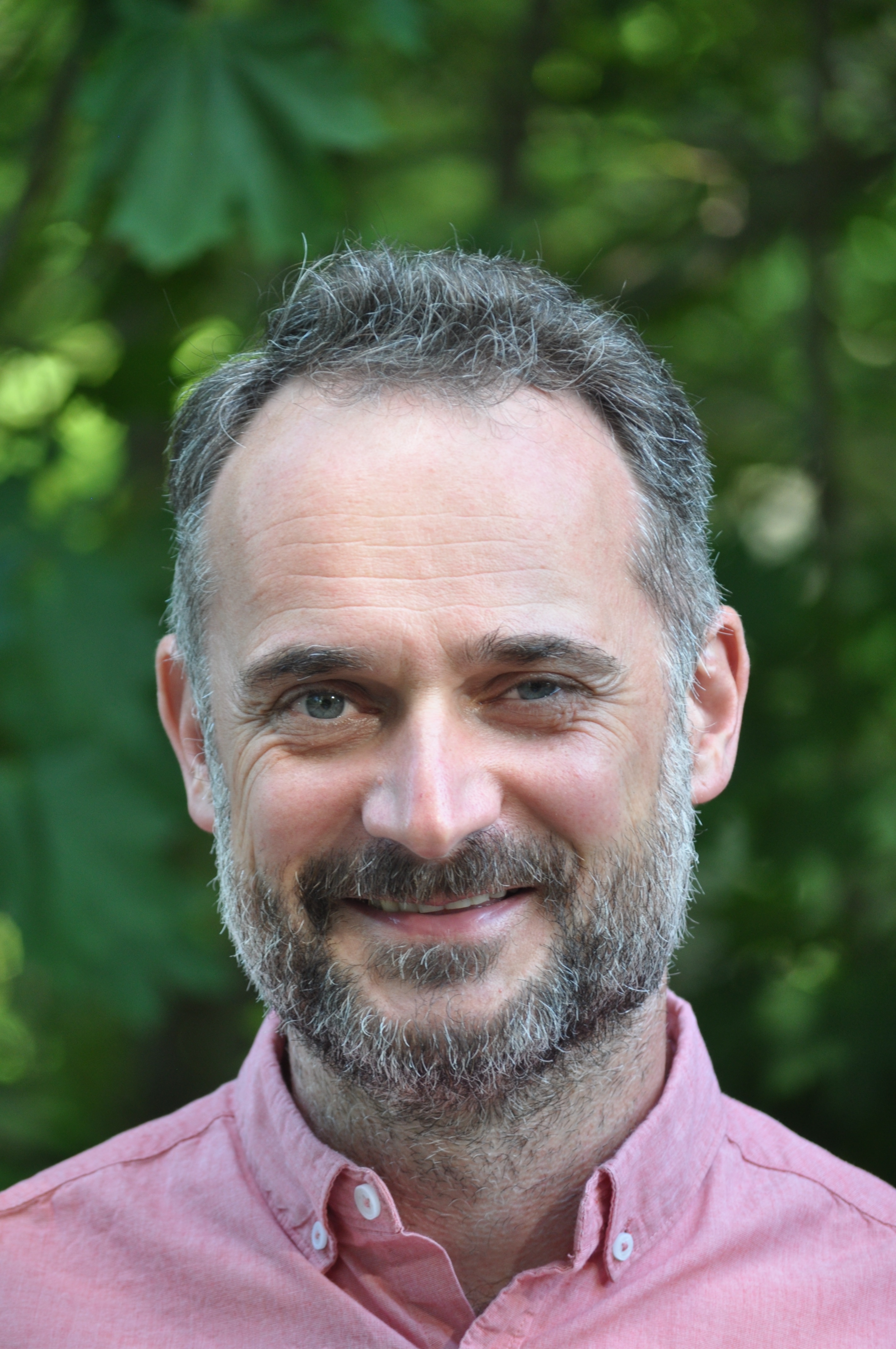 Middle aged man in pink shirt smiles at camera 