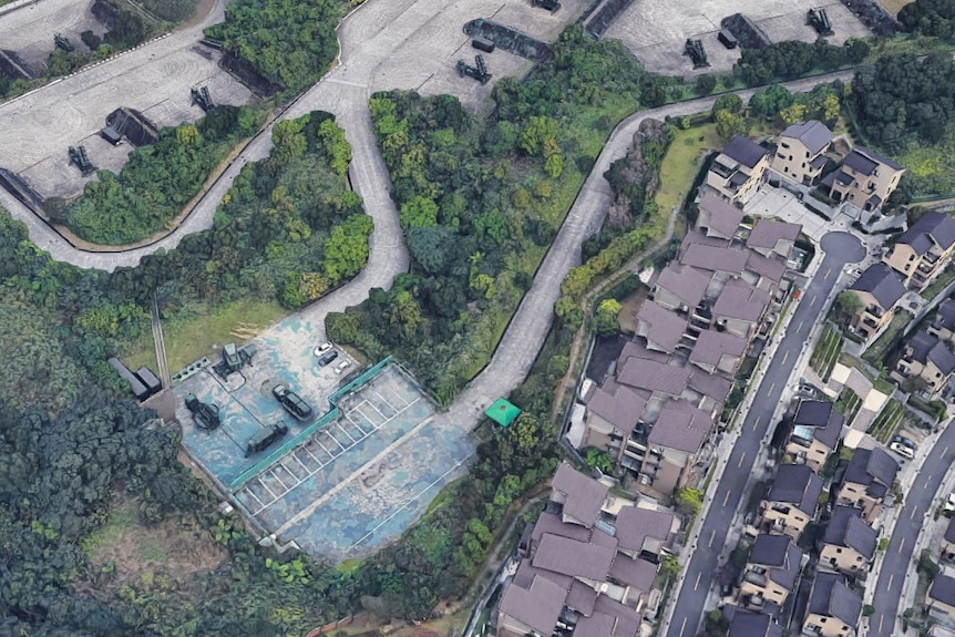 An satellite photo shows rows of houses banked up against a military complex with winding concrete roads.