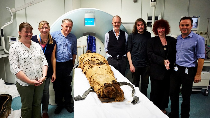 Researchers standing next to a bed with a mummy.