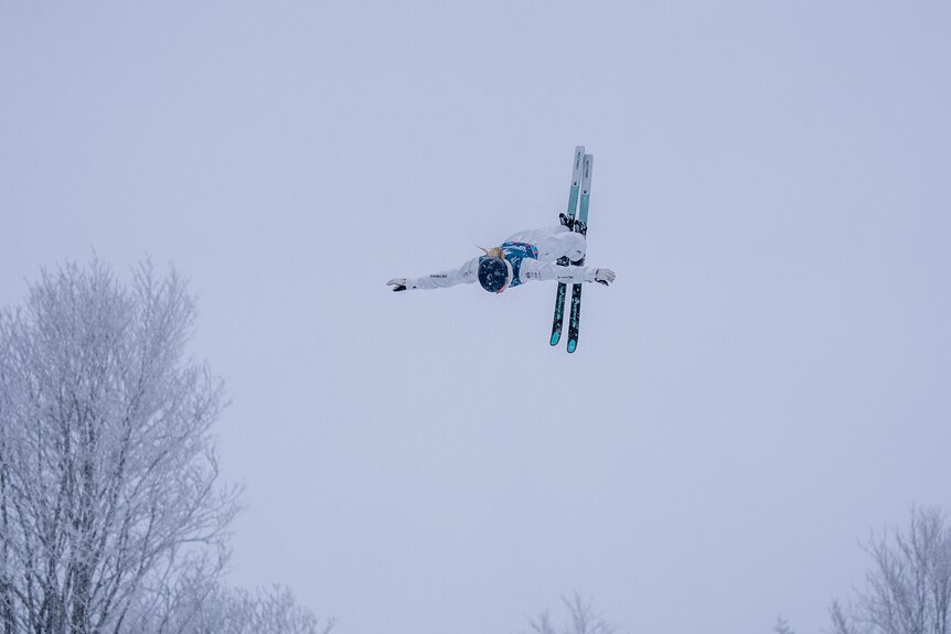 Danielle Scott holds her arms wide and has her skis together as she flips in the snow
