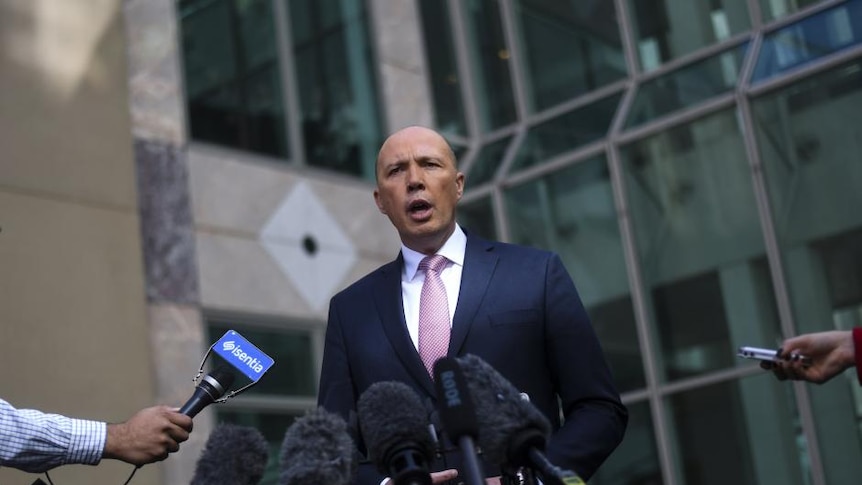 Peter Dutton stands in front of a government building speaking with reporters