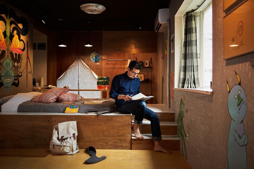 A man sits reading in a neat and tidy loft.