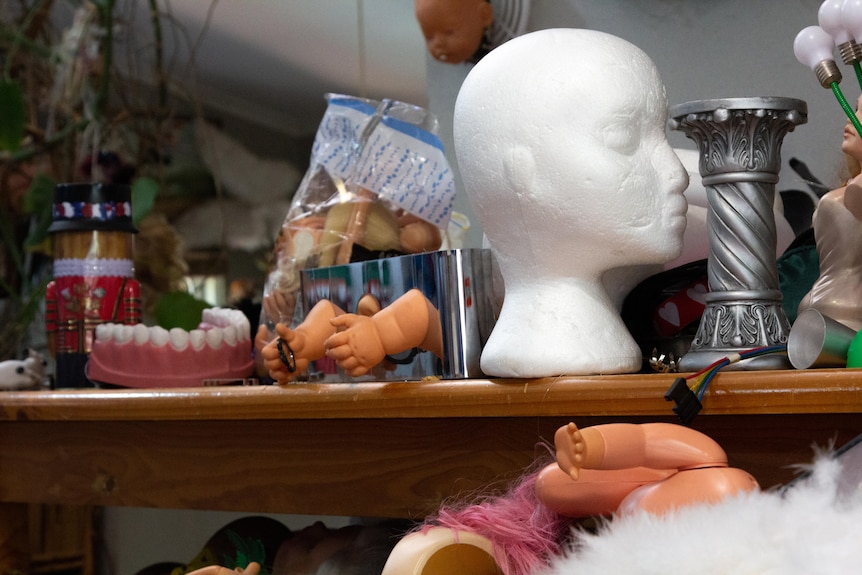 A wooden work table, covered in an assortment of strange items including doll's limbs, big fake teeth, polystyrene head