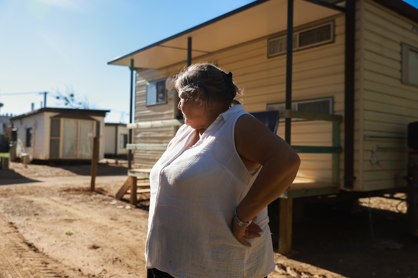 woman looks out over caravan park, holding her arms at her sides in front of cabins  