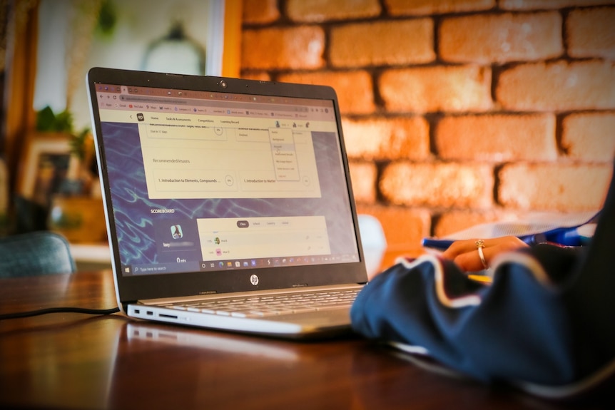 A school student using Education Perfect: Science on their laptop while looking at their phone.