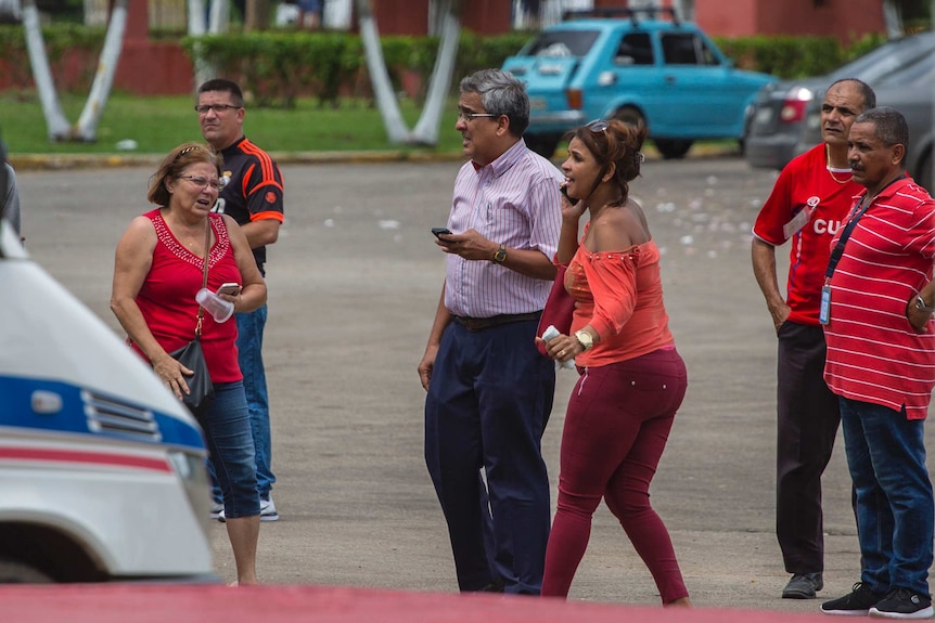 Six people walk or stand in a carport, some look distraught