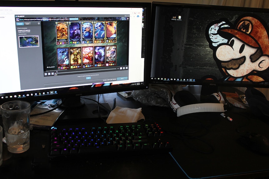 Two computer monitors with video games on them behind a rainbow coloured keyboard.