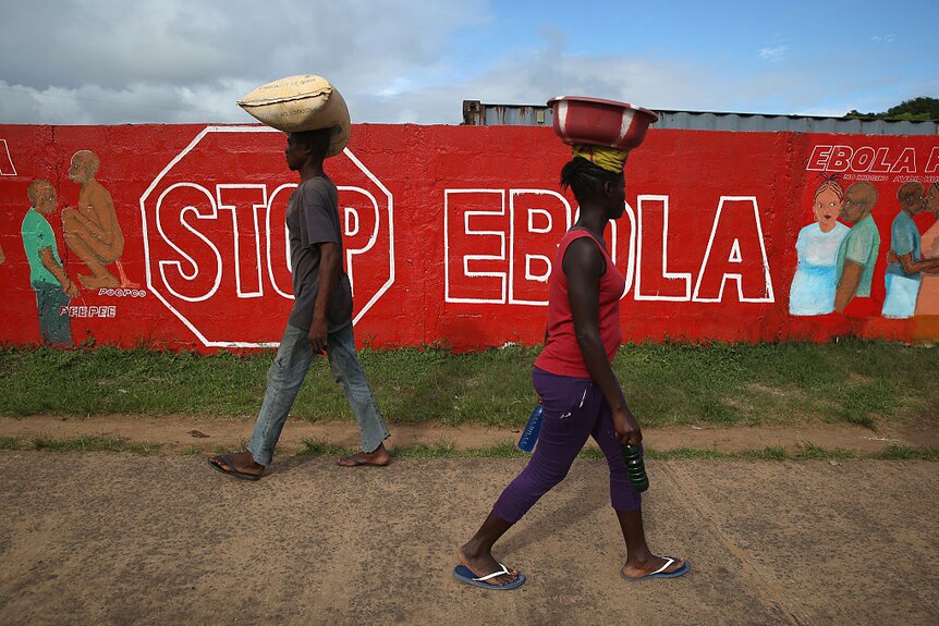Two people walking past a red mural that says "Stop Ebola".