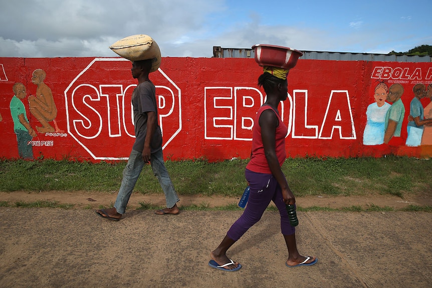 Two people walking past a red mural that says "Stop Ebola".