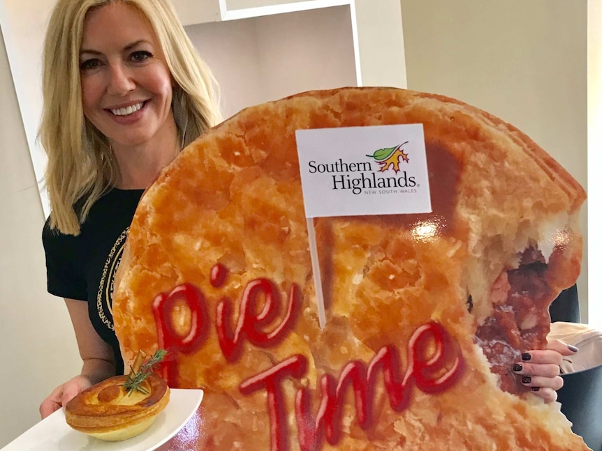 A woman holds a gimmicky over sized pie.