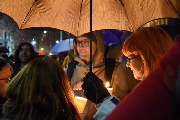 People's faces lit by candles under umbrellas at Melbourne refugee rally