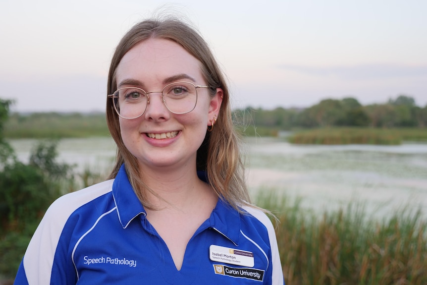 a young woman stands in front of a reedy lagoon