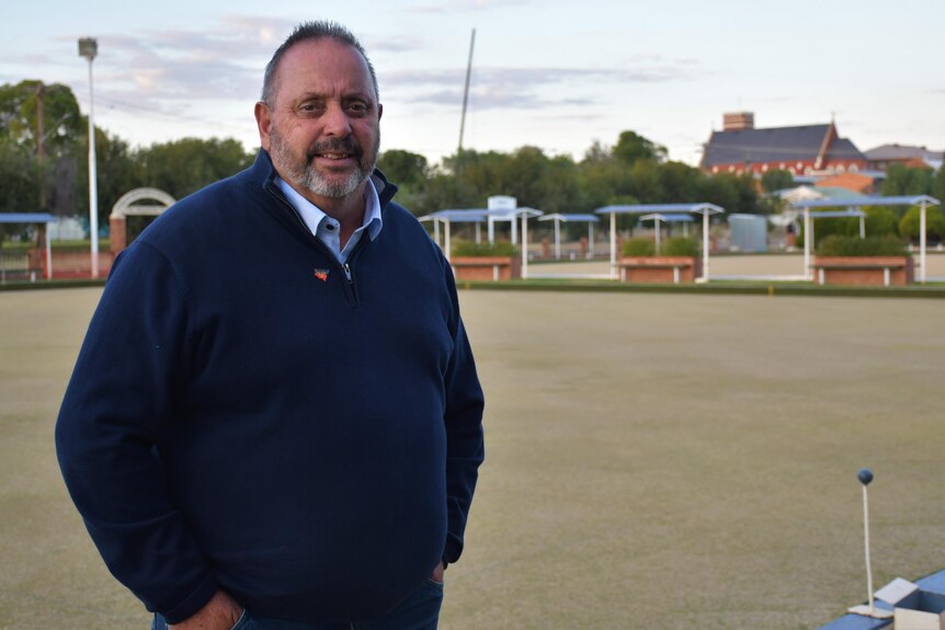An Aboriginal man stands next to a bowling green in a small regional town.