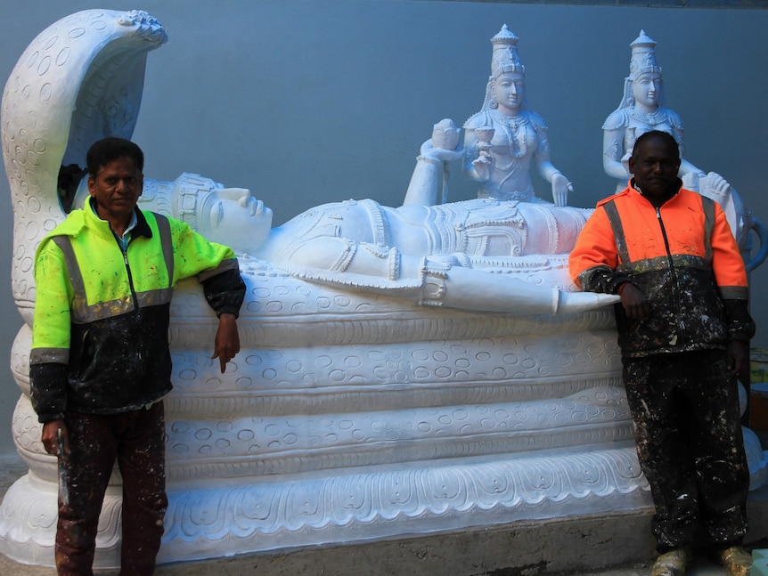 Men in hi vis stand in front of a large white religious statue that is under construction