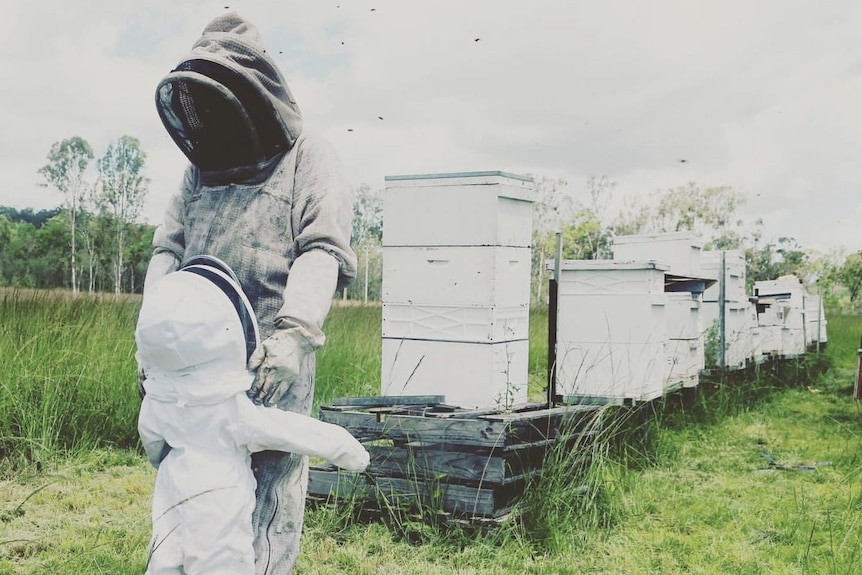 Janine Cannon and her daughter Violet are in beekeeper suits, with a number of hives visible in the background.