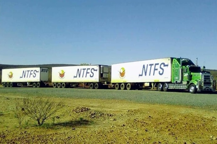 A green Kenworth truck with three trailers attached on a dusty road.