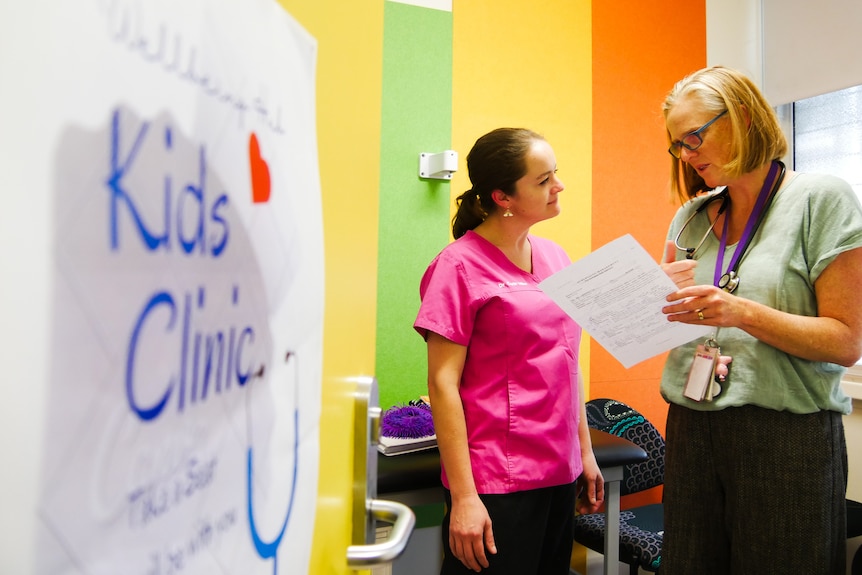 a woman chats with a colleague in a room with 'kids clinic' sign