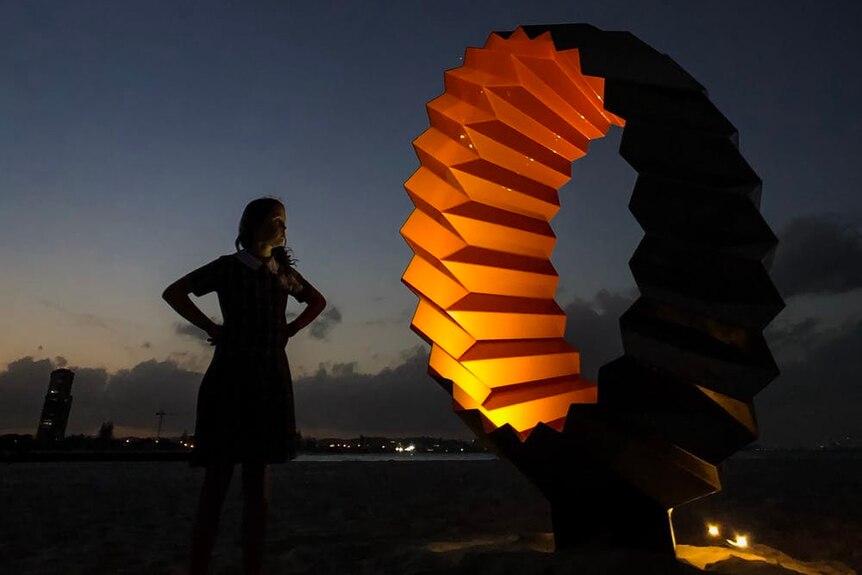 A girl stands in front of a lit up sculpture