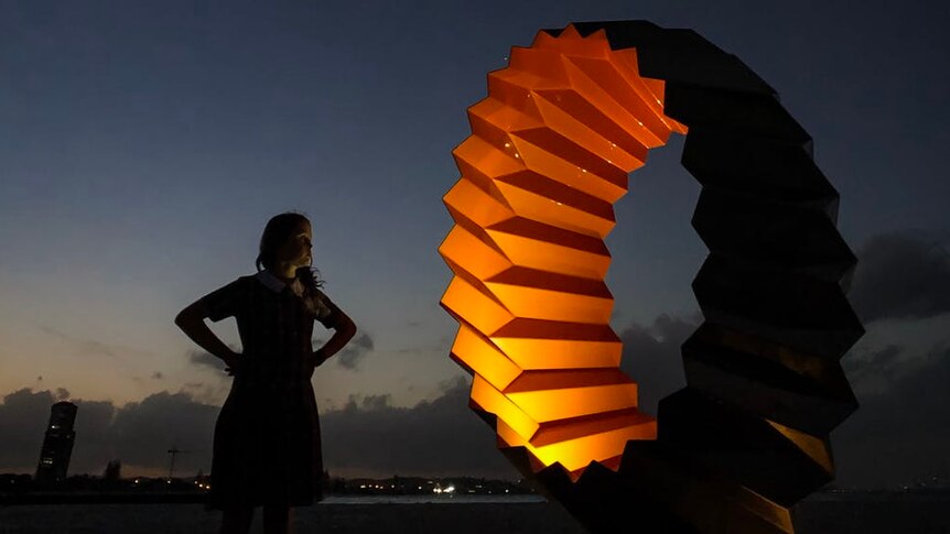 A girl stands in front of a lit up sculpture