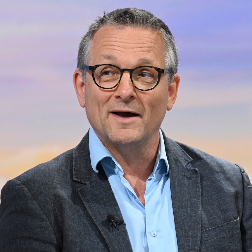 Michael Mosley speaks on a morning talk show wearing a blazer, blue shirt and glasses