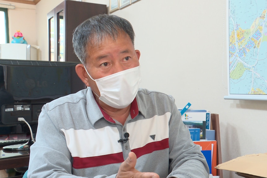 Joon-jae Lee sitting being interviewed in a surgical face mask. 