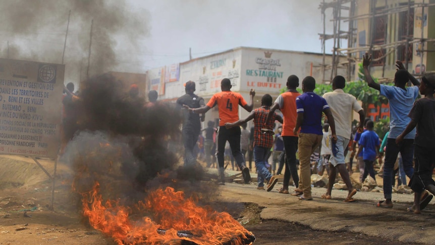 A burning tyre sits beside a row as a group of Congolese men run past with their hands in the air.