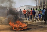 A burning tyre sits beside a row as a group of Congolese men run past with their hands in the air.