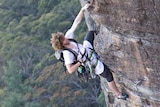 A young man in a climbing harness hanging from a vertical rock face