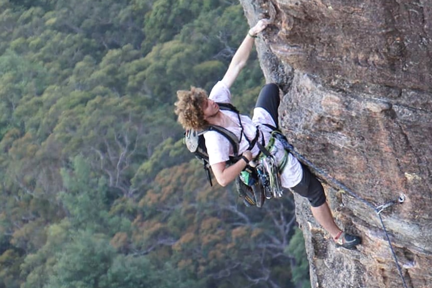A young man in a climbing harness hanging from a vertical rock face