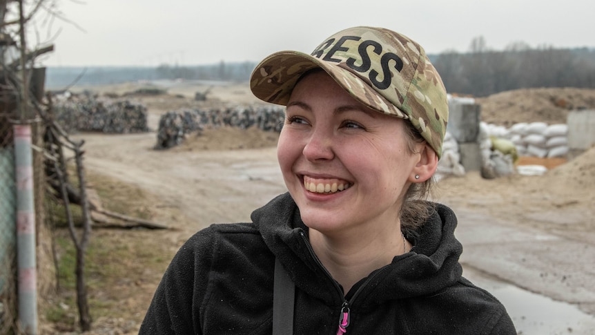 Woman wearing a black jumper and camouflage cap smiling.