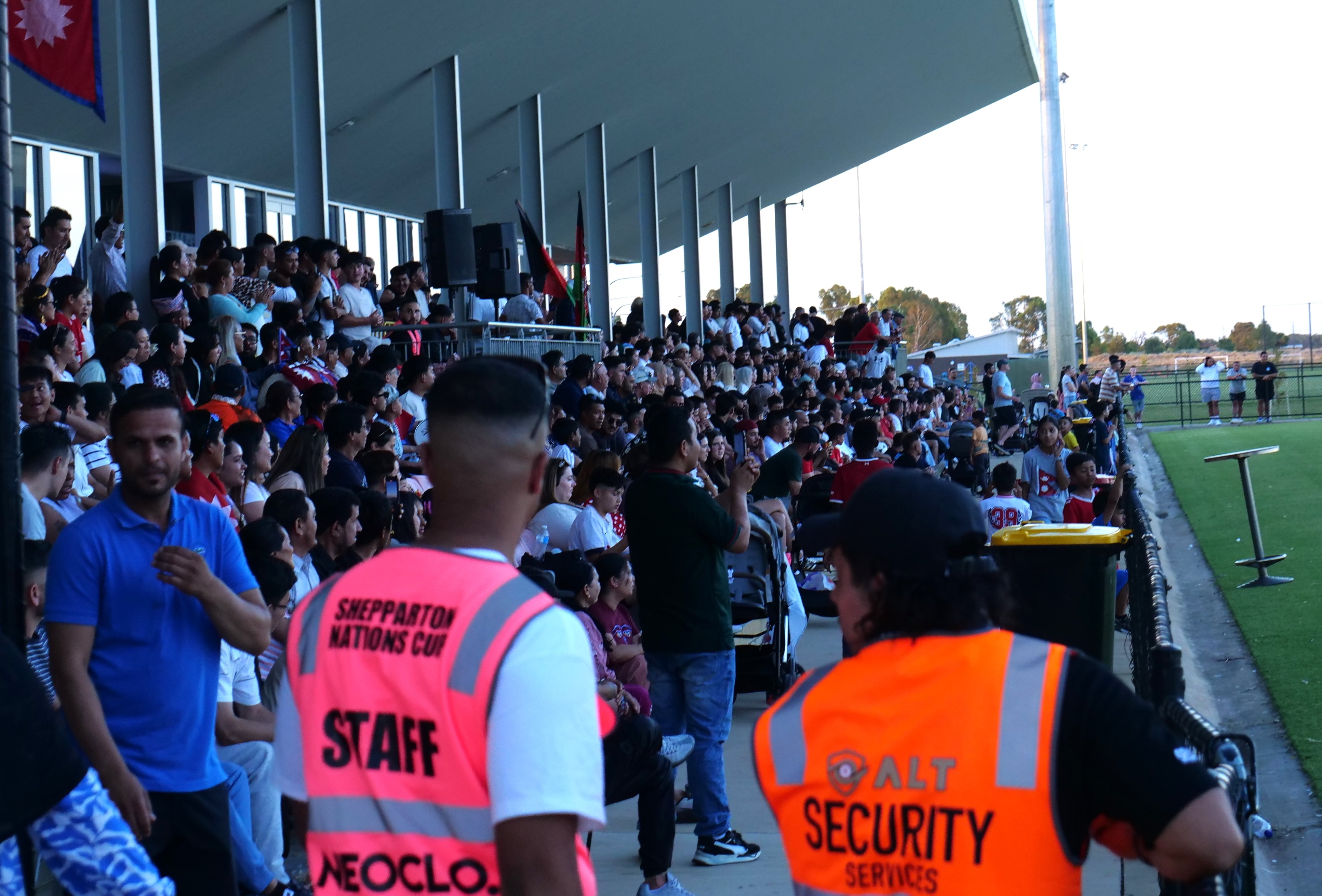 A large crowd sitting on sports benches at a local football pitch