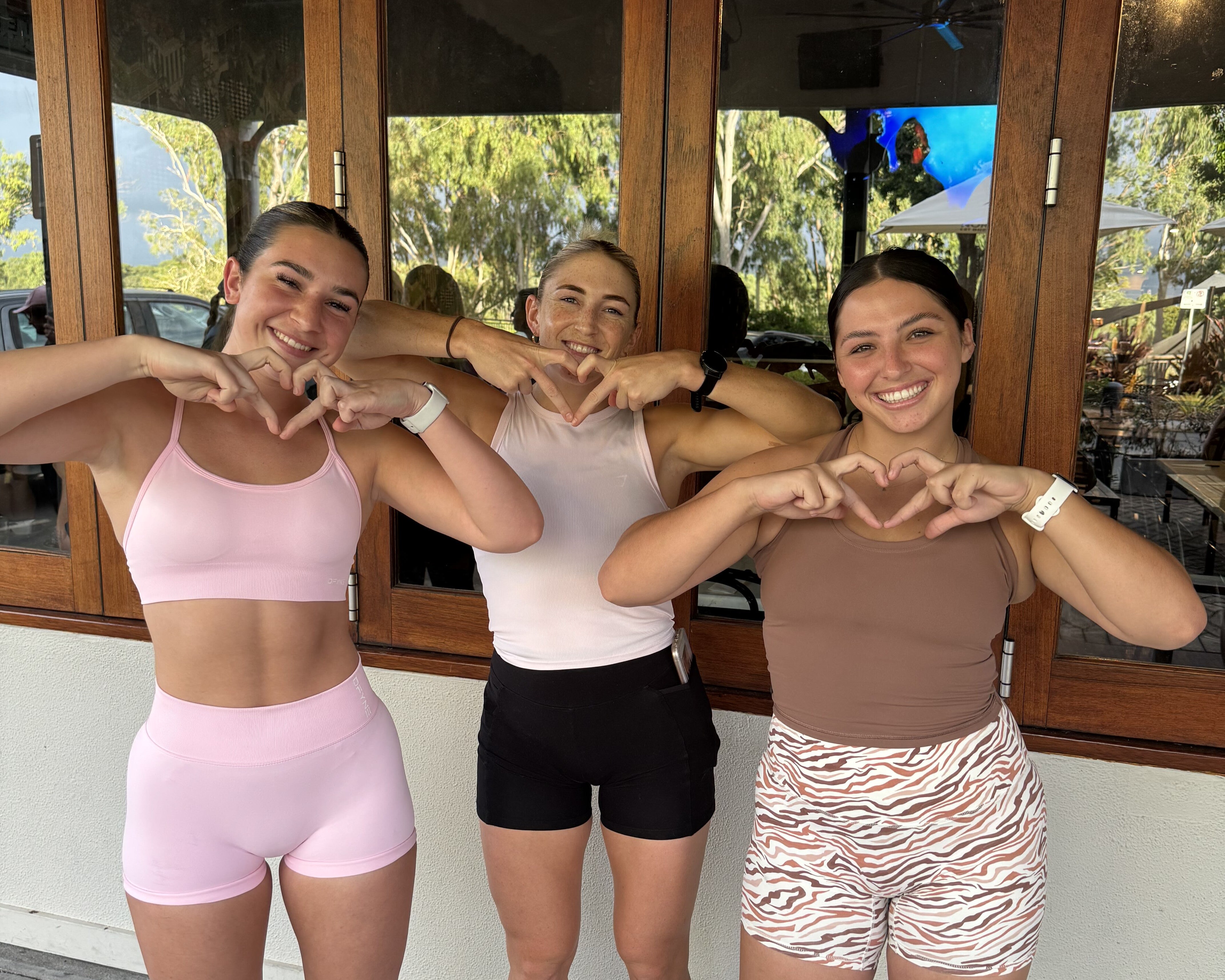 Three girls smile at camera making love heart shape with hands