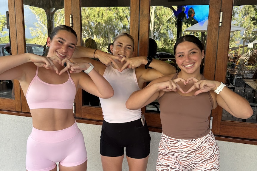 Three girls smile at camera making love heart shape with hands