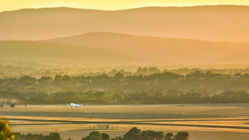 Panorama photo from a distance of a plane, small in the frame, taking off from a rural airport.