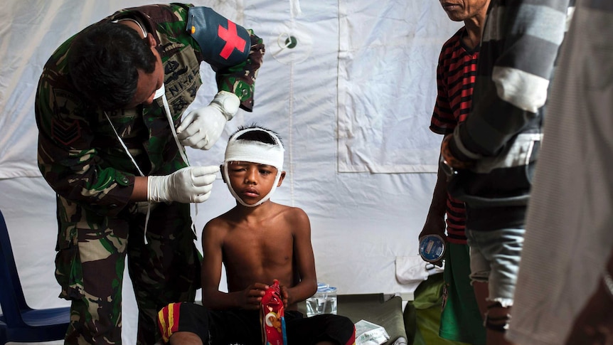 A military paramedic wraps bandages around a boy's head.