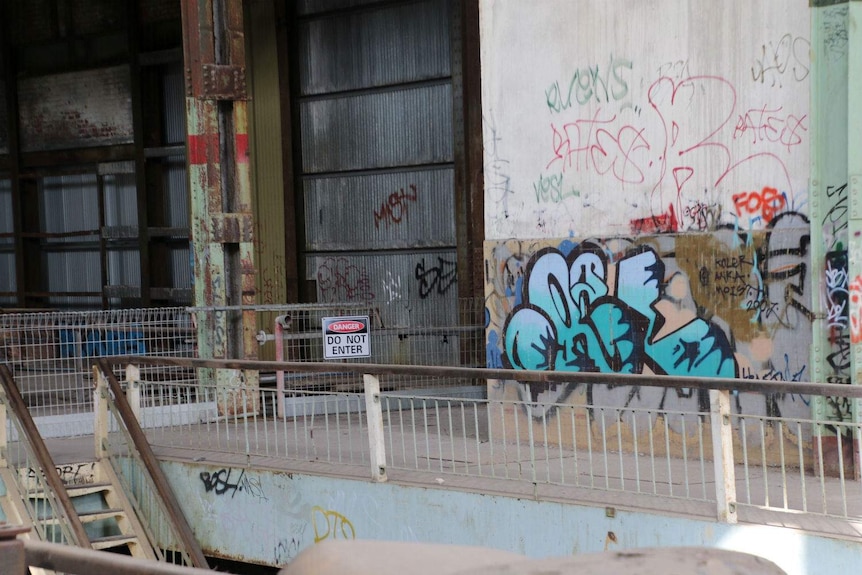The inside of an old power station with graffiti on the walls and a danger sign on a rail.