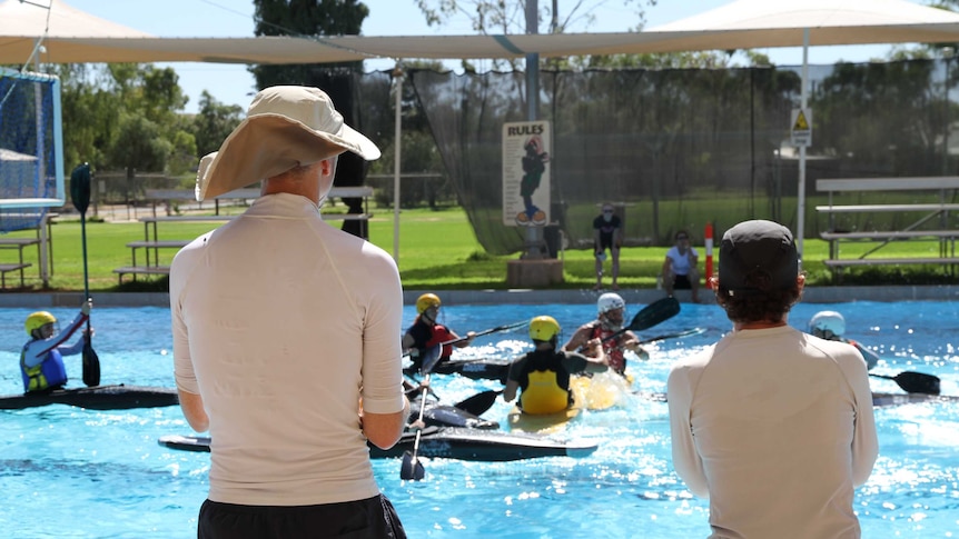 Canoe polo coaches stand by the side of the Alice Springs pool, watching their players train.