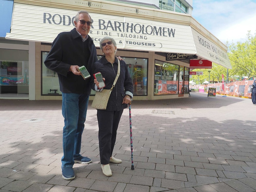 Two older Australians smile and show off their COVIDSafe app