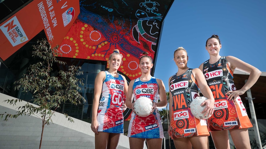 Four players, two from the Swifts, two from the Giants, pose in front of Indigenous artwork on the outside of an area.