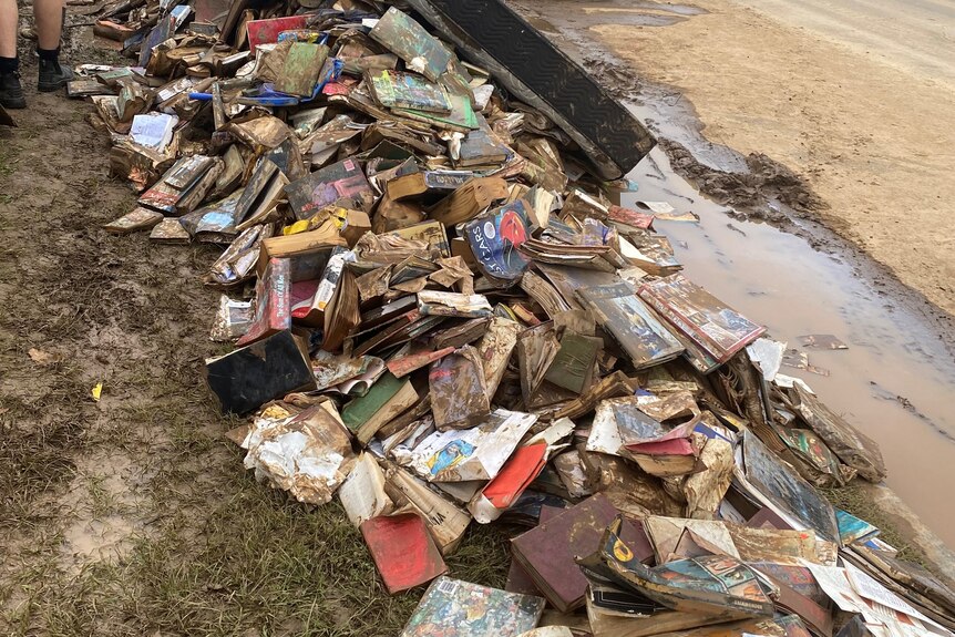 Flood damaged books and debris sit beside a dirt road