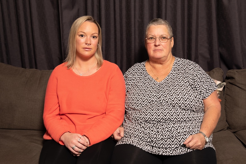 Jessie Orrell and Leonie Riley sit on a couch in front of dark curtains.