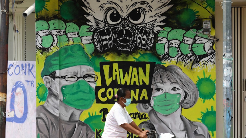 A woman rides her bicycle past a coronavirus awareness mural depicting medical workers in Indonesia.