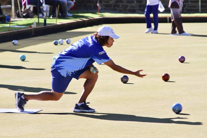 Woman in a blue uniform throws a lawn bowls bowl during a state game.